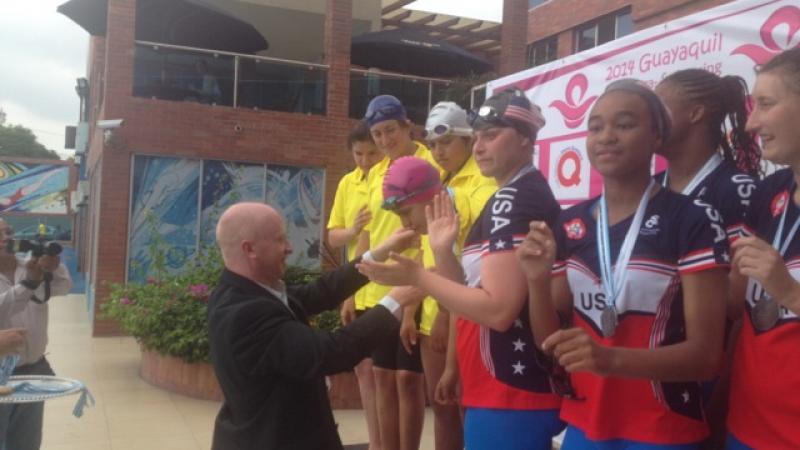 Inas Executive Director at a site visit to Guayaquil, Ecuador, venue for the 2015 Inas Global Games. Man in black suit putting a medal around a young girls neck