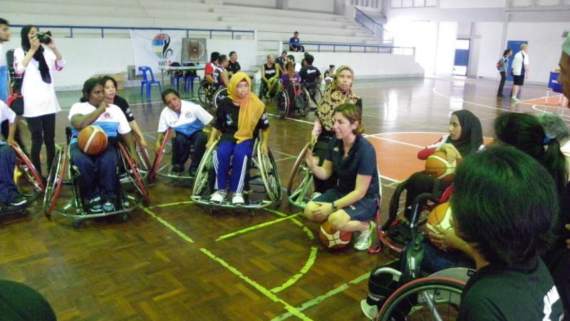 Wheelchair basketball women's camp - Thailand A coach kneels while women in wheelchairs gather around her