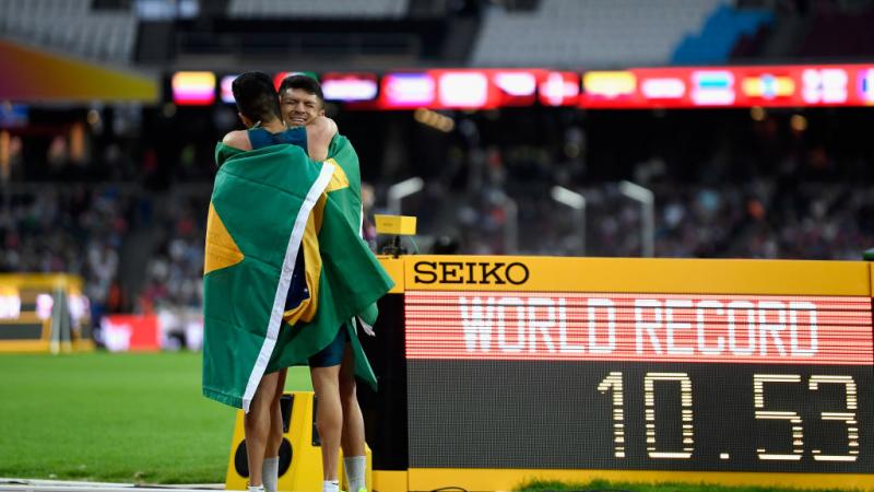 Petrucio Ferreira - Yohansson Nascimento - Brazil - London 2017 Two athletes hug on the track in front of a bulletin board showing 'WR'