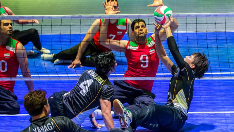 Iran vs Japan - sitting volleyball Japanese sitting volleyball player sets the ball while an Iranian athlete prepares to block
