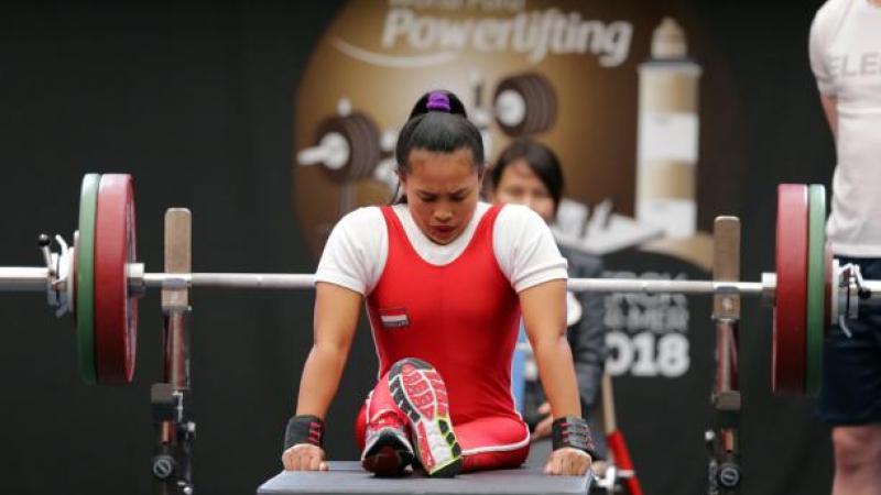 Ni Nengah Widiasih - Indonesia - powerlifting Woman bows head as she sits on powerlifting bench preparing to lift the bar