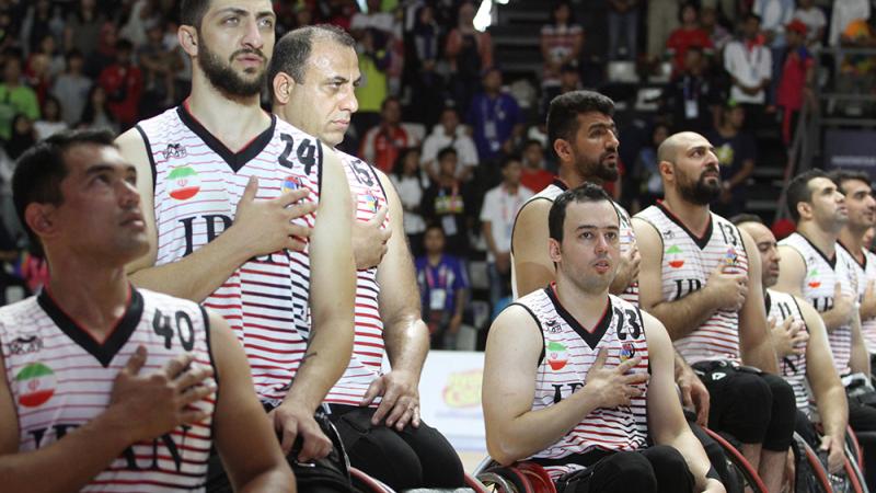 Iran men's wheelchair basketball - Indonesia 2018 male wheelchair basketball players with Iran on their shirt holding their hands over their heart and singing