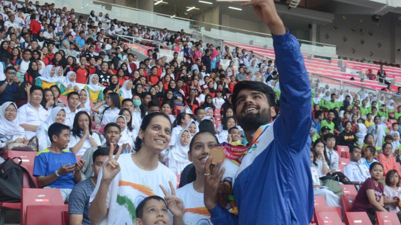 Sandeep Chaudhary - India - Para athletics - Asian Para Games 2018 Man with a medal taking pictures with fans on the stands in a stadium