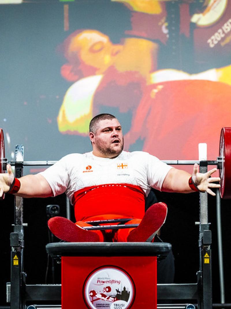 A male powerlifter in a bench press with two men standing next to him