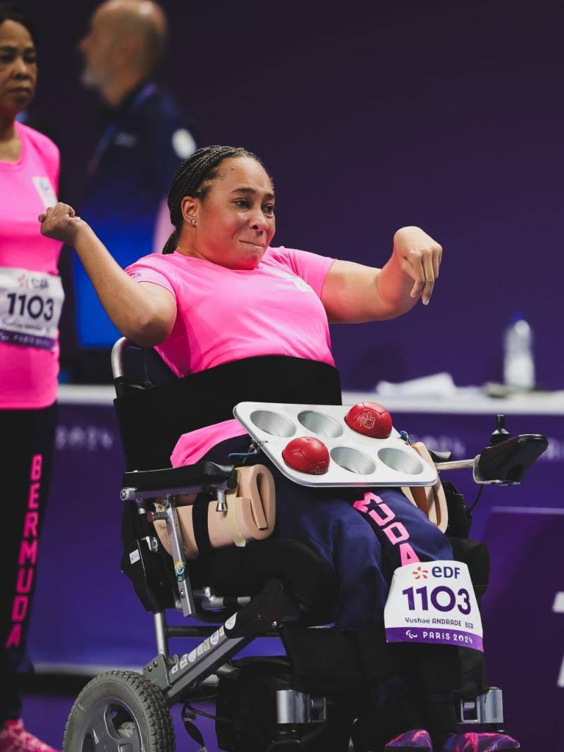 A female boccia athlete wearing a pink uniform is throwing a red boccia ball
