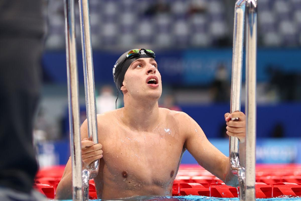A male Para swimmer is using the handrails to leave the pool after a competition