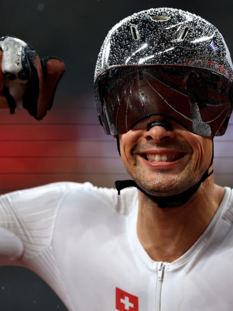Switzerland's Marcel Hug wears a silver helmet that is shining with rain droplets and raises his hands to celebrate his victory in the men’s 800m T54 final