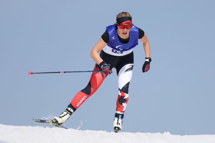 A female athlete wearing a black T-shirt and blue bibs is in skiing 