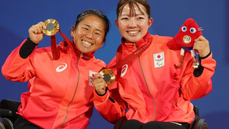 Two female athletes celebrate on the podium with gold medal