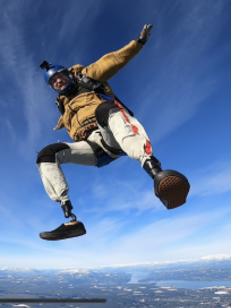 A male athlete is posing for a photo by opening his arms wide while skydiving